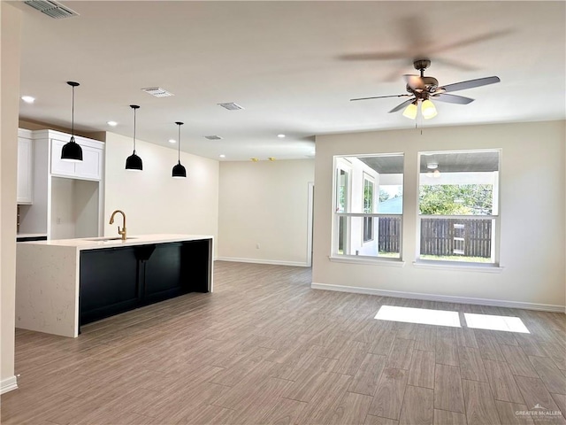 kitchen featuring ceiling fan, sink, light hardwood / wood-style flooring, a center island with sink, and white cabinets