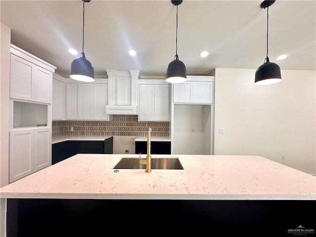 kitchen with decorative backsplash, an island with sink, white cabinets, and pendant lighting