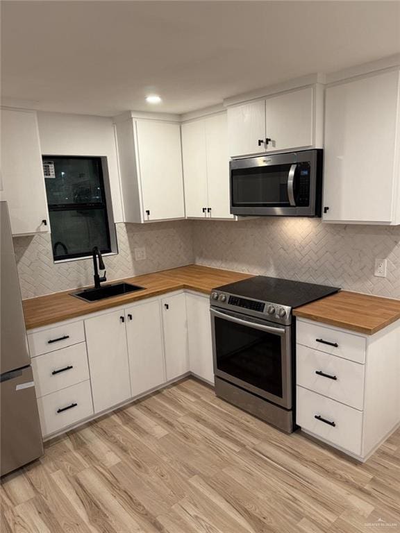 kitchen featuring appliances with stainless steel finishes, light wood-style floors, a sink, and wood counters