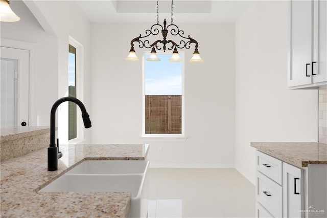 kitchen with light stone countertops, sink, hanging light fixtures, white cabinets, and light tile patterned flooring