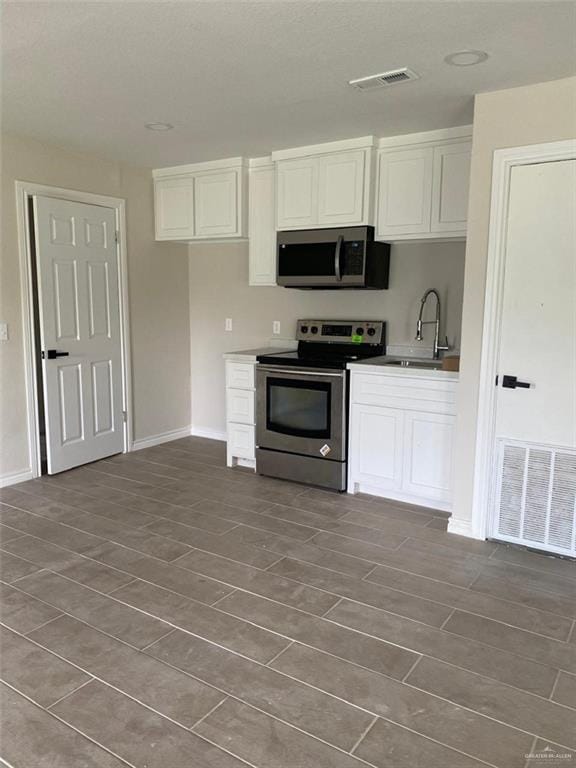 kitchen with appliances with stainless steel finishes, white cabinetry, and sink