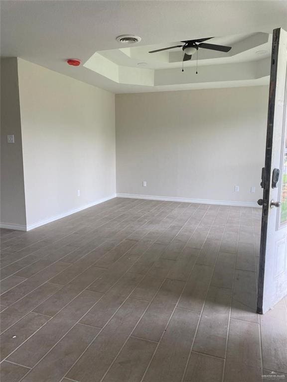 unfurnished room featuring a tray ceiling, ceiling fan, and dark hardwood / wood-style flooring