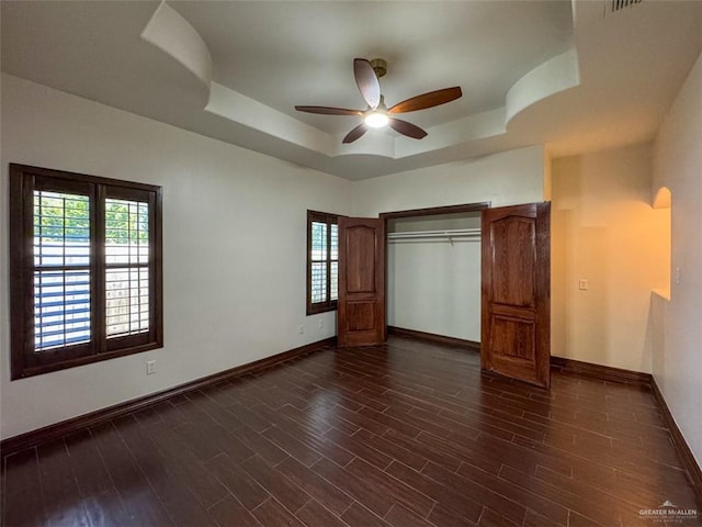 unfurnished bedroom with a raised ceiling, baseboards, multiple windows, and dark wood-style flooring