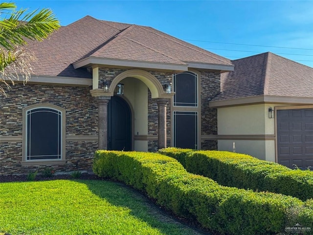 french provincial home with a garage, a front yard, stucco siding, stone siding, and roof with shingles