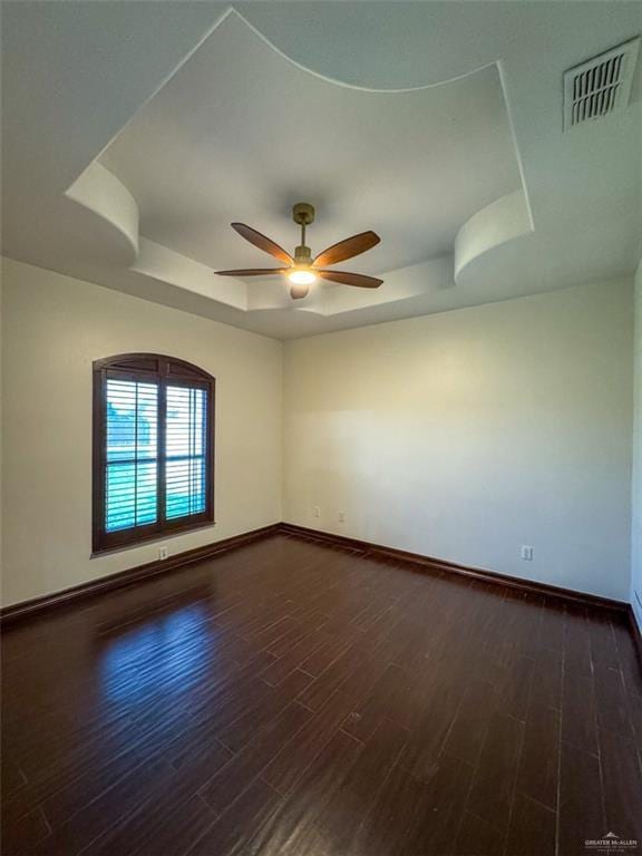 spare room with a tray ceiling, baseboards, dark wood finished floors, and ceiling fan