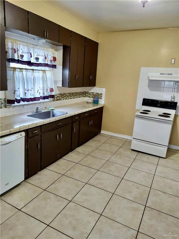 kitchen featuring decorative backsplash, dark brown cabinetry, white appliances, and sink