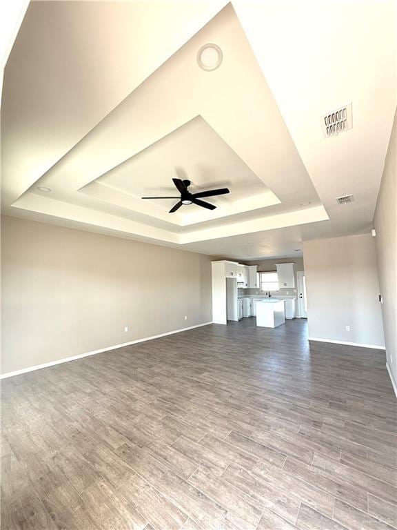 unfurnished living room featuring dark wood-type flooring, visible vents, a raised ceiling, and a ceiling fan