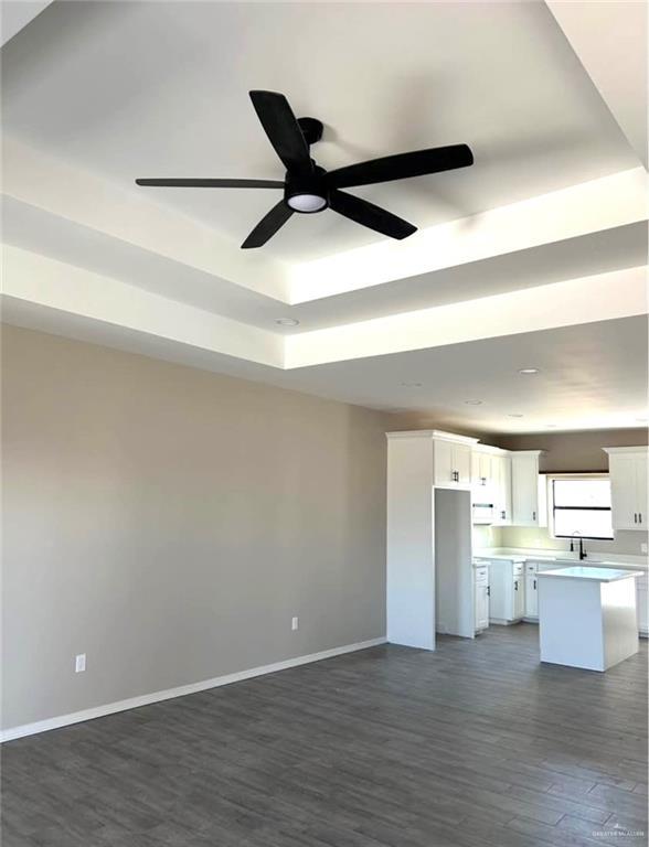 unfurnished living room with dark hardwood / wood-style floors, ceiling fan, a raised ceiling, and sink