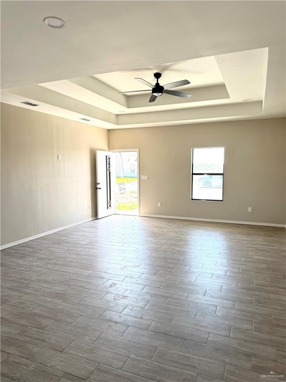 spare room featuring dark wood-type flooring, a raised ceiling, ceiling fan, and baseboards