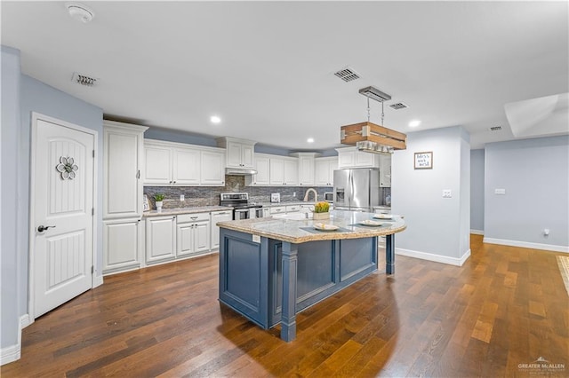 23807 Stuart Place Rd, Harlingen, TX 78552 - kitchen featuring stainless steel appliances, white cabinets, under cabinet range hood, dark wood-type flooring, and backsplash