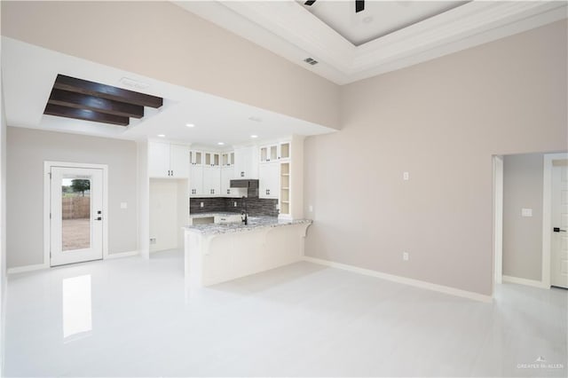 kitchen featuring light stone counters, a peninsula, white cabinets, a tray ceiling, and glass insert cabinets