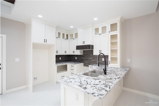 kitchen featuring under cabinet range hood, a sink, white cabinetry, decorative backsplash, and glass insert cabinets