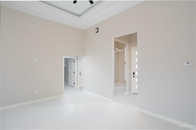 spare room featuring baseboards, a raised ceiling, ceiling fan, ornamental molding, and a high ceiling