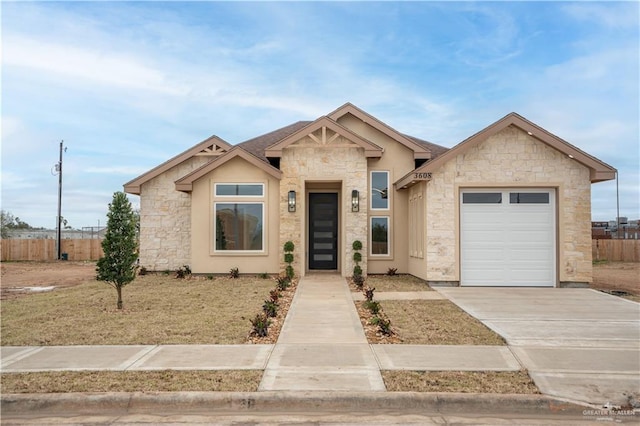 view of front facade with stone siding, fence, driveway, and an attached garage