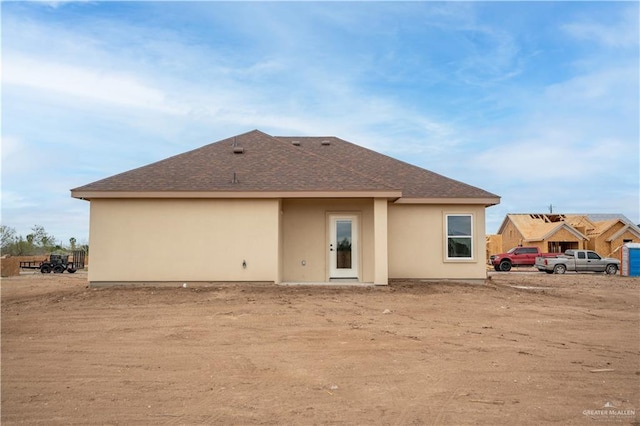 rear view of property featuring a shingled roof and stucco siding