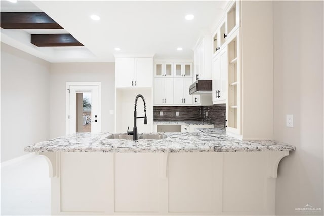 kitchen with light stone counters, glass insert cabinets, white cabinetry, a sink, and a peninsula