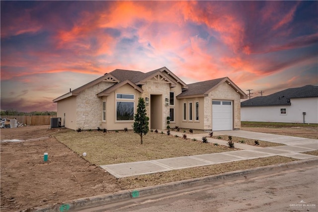 view of front of home featuring an attached garage, stone siding, central AC, and concrete driveway