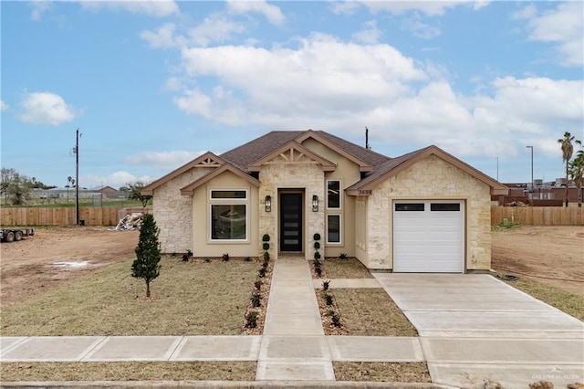 view of front of house with driveway, stone siding, an attached garage, and fence