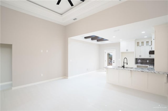 kitchen featuring glass insert cabinets, white cabinetry, a sink, light stone countertops, and baseboards