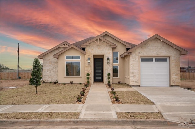 view of front facade with stone siding, concrete driveway, fence, and an attached garage