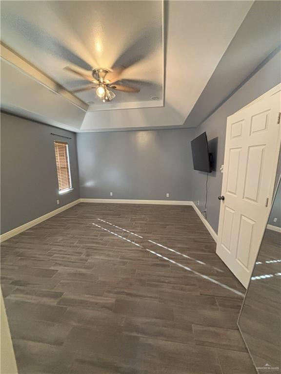 interior space with a raised ceiling, ceiling fan, and dark hardwood / wood-style floors