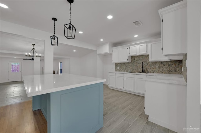 kitchen featuring white cabinets, backsplash, sink, and hanging light fixtures