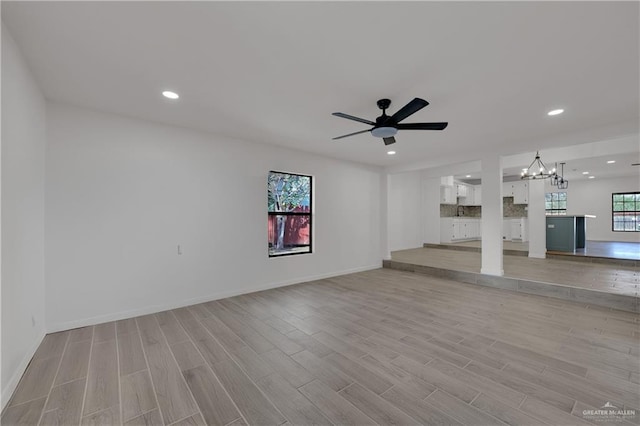 unfurnished living room featuring light hardwood / wood-style flooring, a healthy amount of sunlight, and ceiling fan with notable chandelier