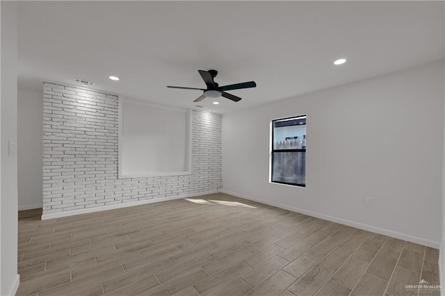 empty room featuring ceiling fan and brick wall