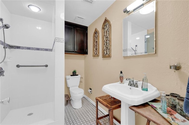 full bathroom with toilet, tiled shower, and baseboards