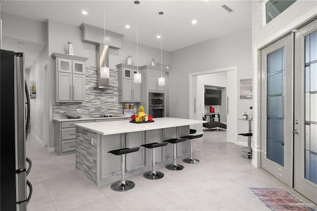 kitchen with pendant lighting, gray cabinets, wall chimney range hood, and appliances with stainless steel finishes