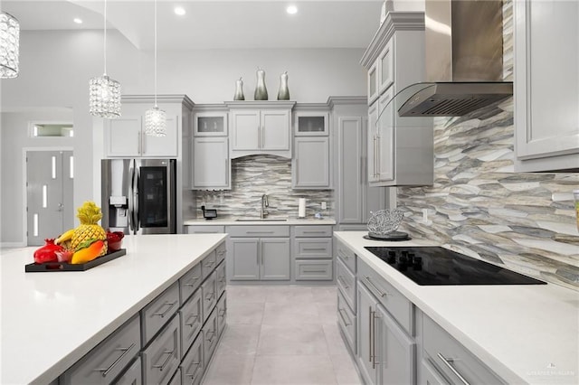 kitchen with sink, stainless steel refrigerator with ice dispenser, hanging light fixtures, wall chimney exhaust hood, and gray cabinets