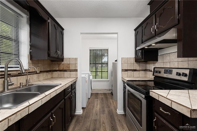 20538 Rio Rancho Rd, Harlingen, TX 78552 - kitchen with stainless steel electric stove, washer and dryer, under cabinet range hood, tile counters, and dark wood-type flooring