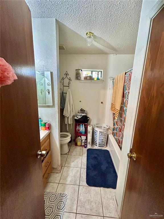 full bathroom with tile patterned flooring, a textured ceiling, toilet, shower / bath combo with shower curtain, and vanity