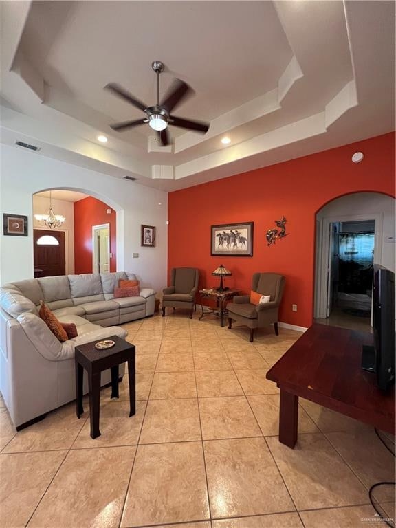 living room with light tile patterned floors, ceiling fan with notable chandelier, and a raised ceiling