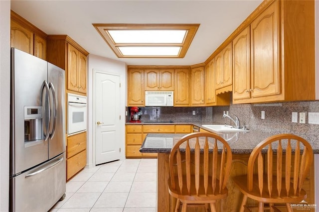 kitchen with sink, white appliances, light tile patterned floors, a kitchen bar, and kitchen peninsula