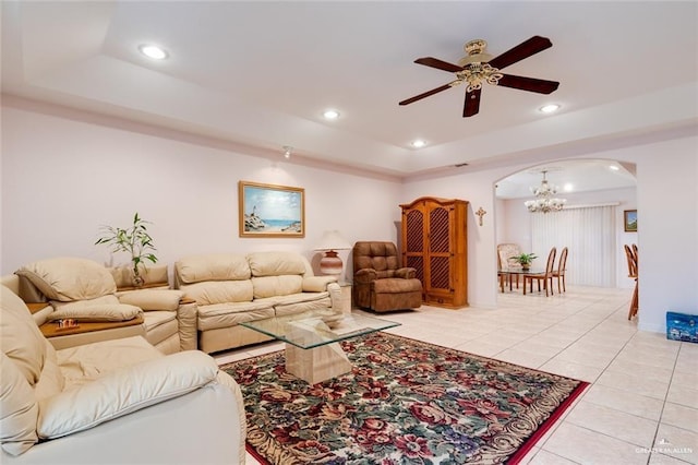 tiled living room with a raised ceiling and ceiling fan with notable chandelier