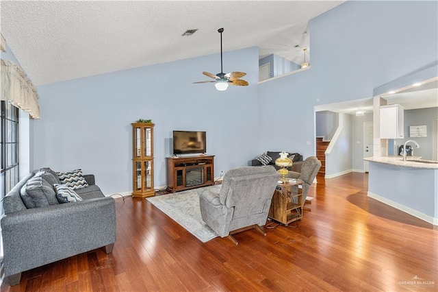 living room featuring visible vents, a textured ceiling, wood finished floors, high vaulted ceiling, and baseboards