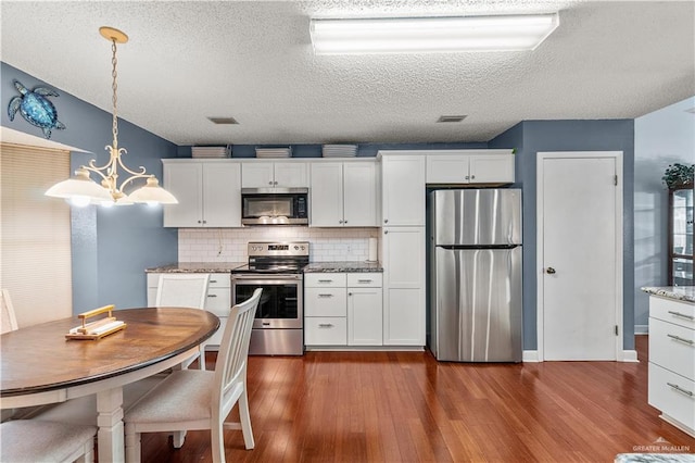 kitchen featuring light stone counters, appliances with stainless steel finishes, white cabinetry, and pendant lighting