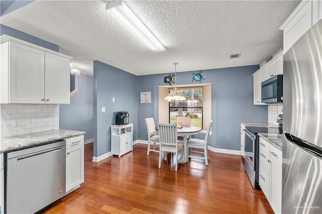 kitchen with light stone countertops, white cabinetry, stainless steel appliances, and dark wood finished floors