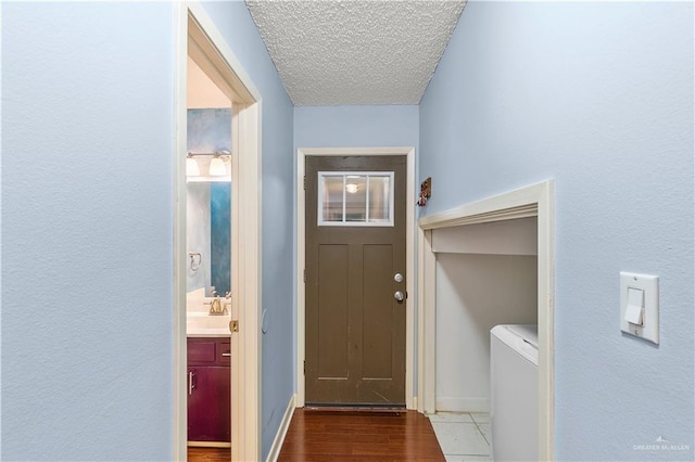 doorway with a sink, a textured ceiling, wood finished floors, washer / dryer, and baseboards