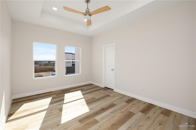 unfurnished room featuring light hardwood / wood-style flooring, ceiling fan, and a tray ceiling