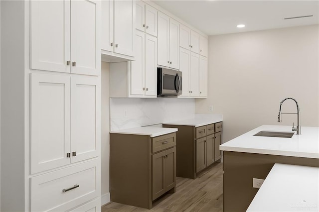 kitchen with sink, backsplash, light hardwood / wood-style flooring, and white cabinets