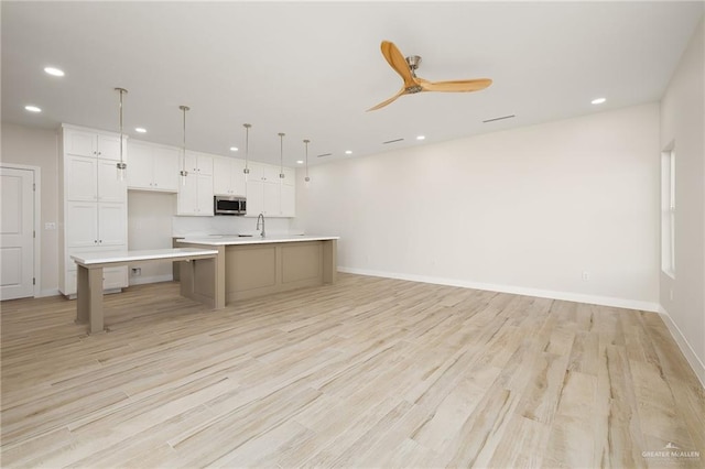 kitchen with a spacious island, white cabinetry, light hardwood / wood-style floors, and hanging light fixtures