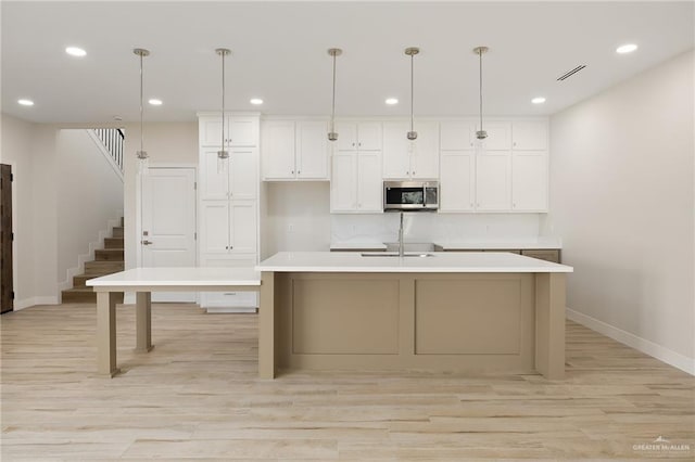 kitchen featuring decorative light fixtures, white cabinetry, sink, a kitchen island with sink, and light wood-type flooring