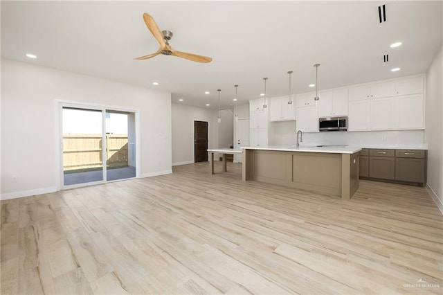 kitchen with pendant lighting, white cabinetry, ceiling fan, light wood-type flooring, and a spacious island