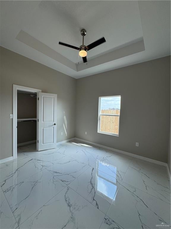 unfurnished bedroom featuring a spacious closet, ceiling fan, and a tray ceiling