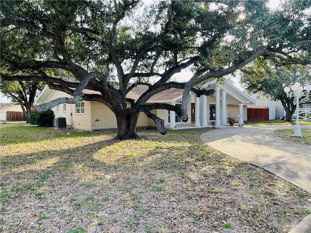 view of front of property with central AC unit, brick siding, fence, driveway, and a front yard