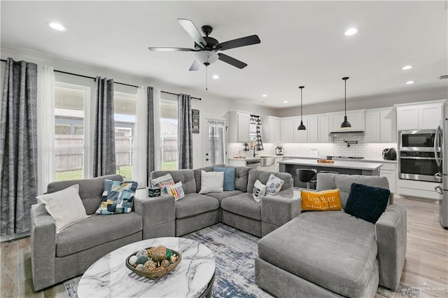 living room featuring light wood-type flooring, ceiling fan, and ornamental molding