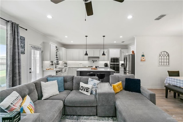 living room with ceiling fan, sink, light wood-type flooring, and crown molding