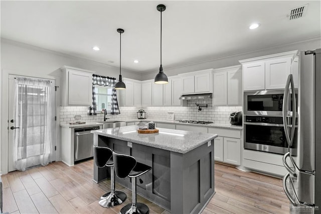 kitchen with light stone countertops, a kitchen island, white cabinets, and appliances with stainless steel finishes